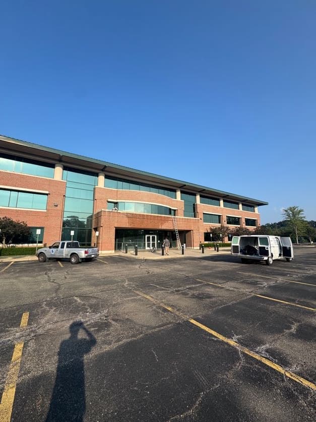 Super Shine Services technician cleaning a commercial office building with a truck and van on site