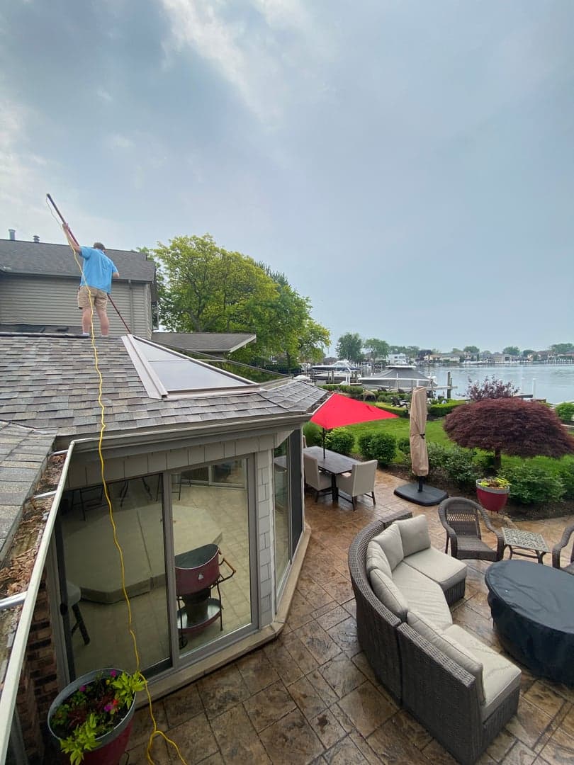 Super Shine Services technician cleaning a roof and solar panels above a lakefront patio