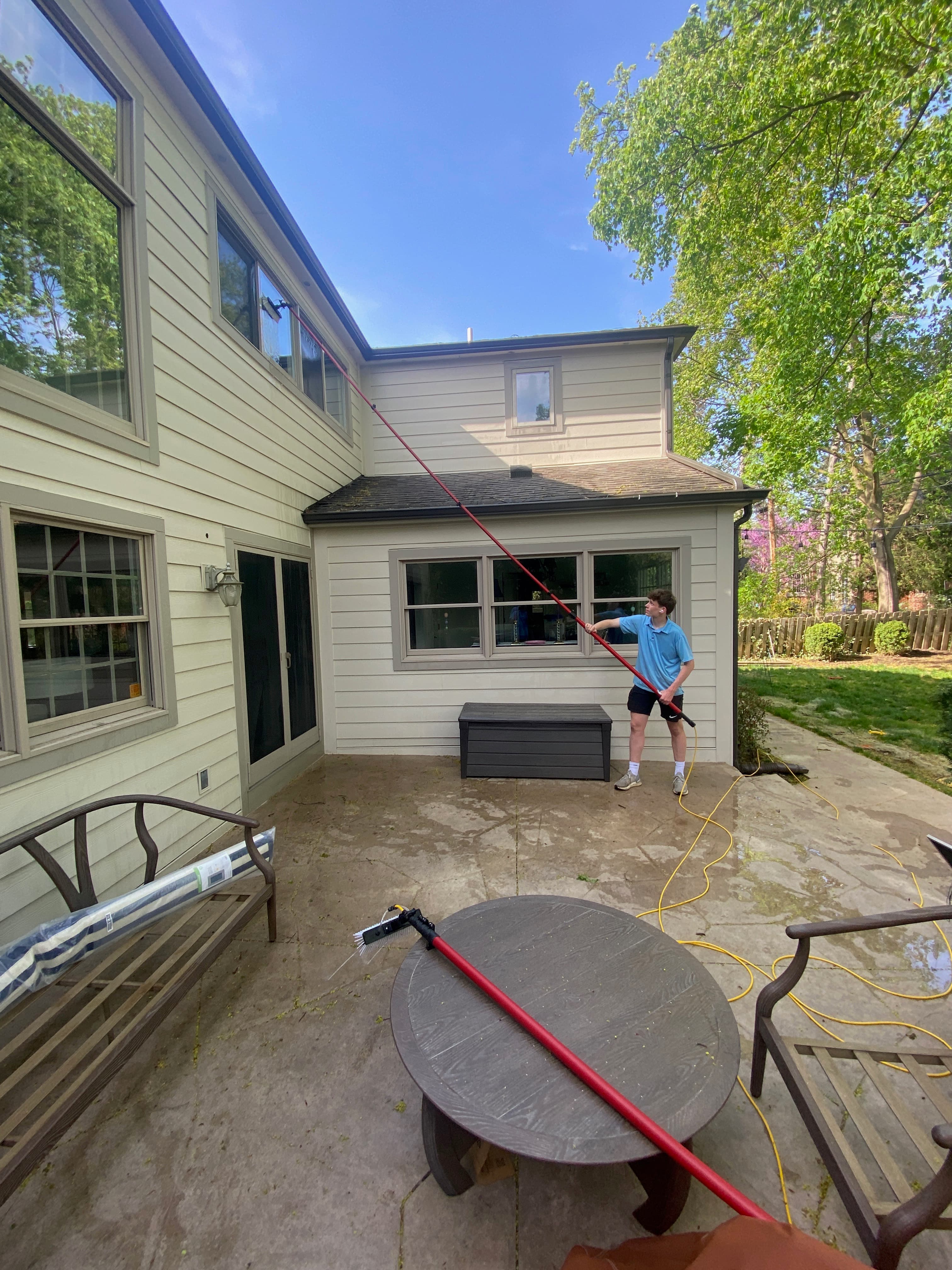 Super Shine Services technician cleaning patio windows and screens on a backyard deck with a hose