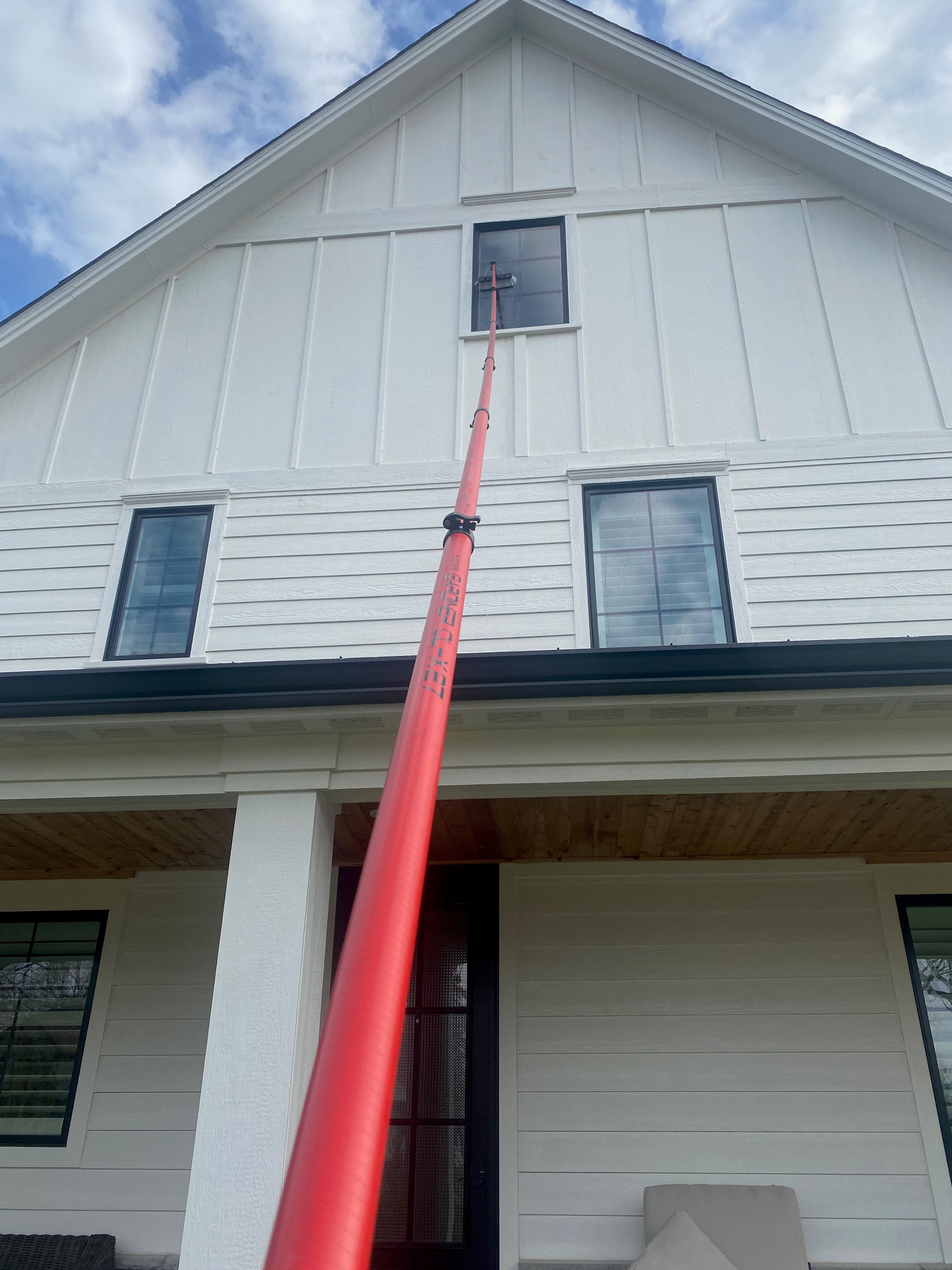 Super Shine Services technician cleaning upper-story windows on a large home exterior with an extension pole